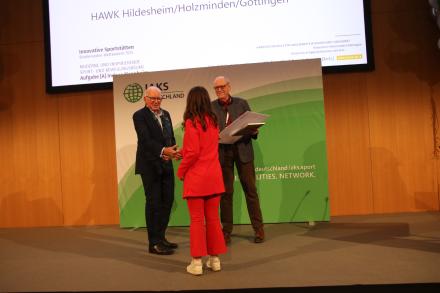 3 Leute schütteln Hände auf Bühne