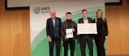 Studierenden lächeln mit Check und Urkunde in die Kamera