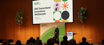 Robin Kähler steht auf der Bühne im Hintergrund Folie mit "Innovations-Wettbewerb" angeschlagen