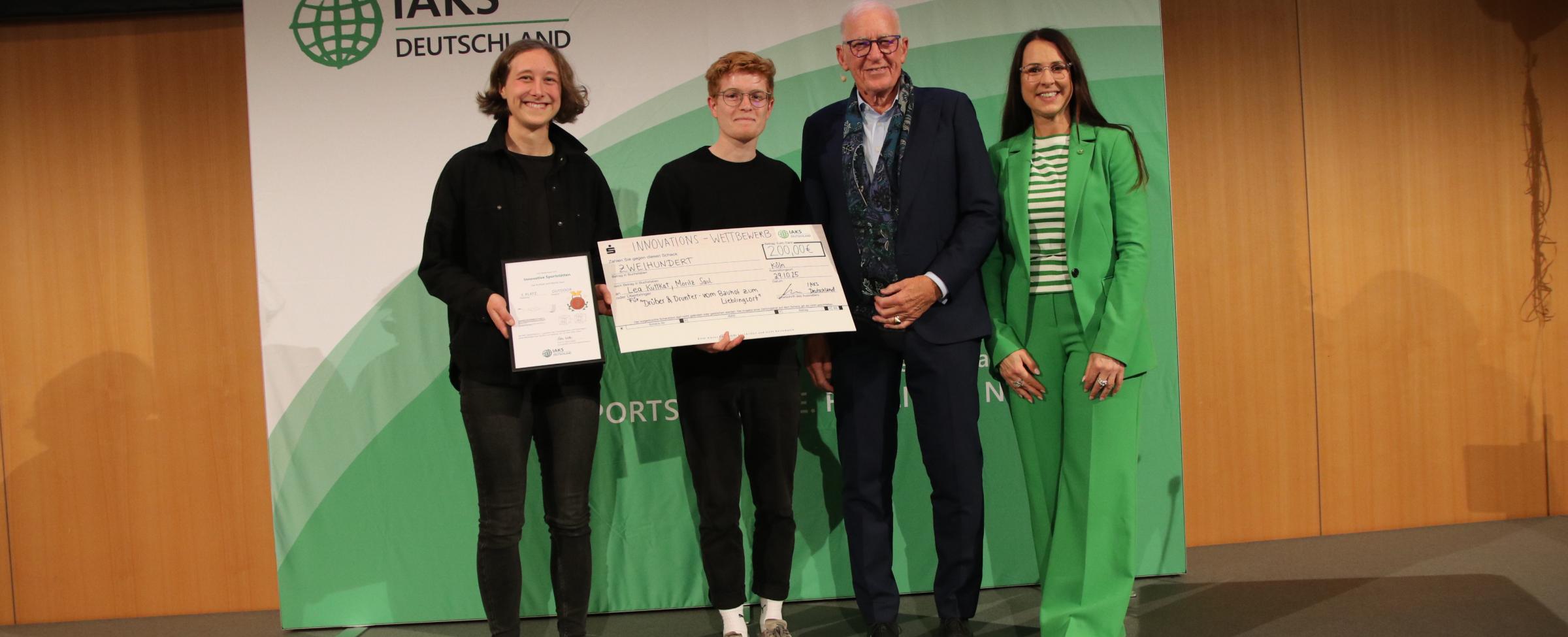 3 Menschen auf Bühne mit Urkunde und Scheck