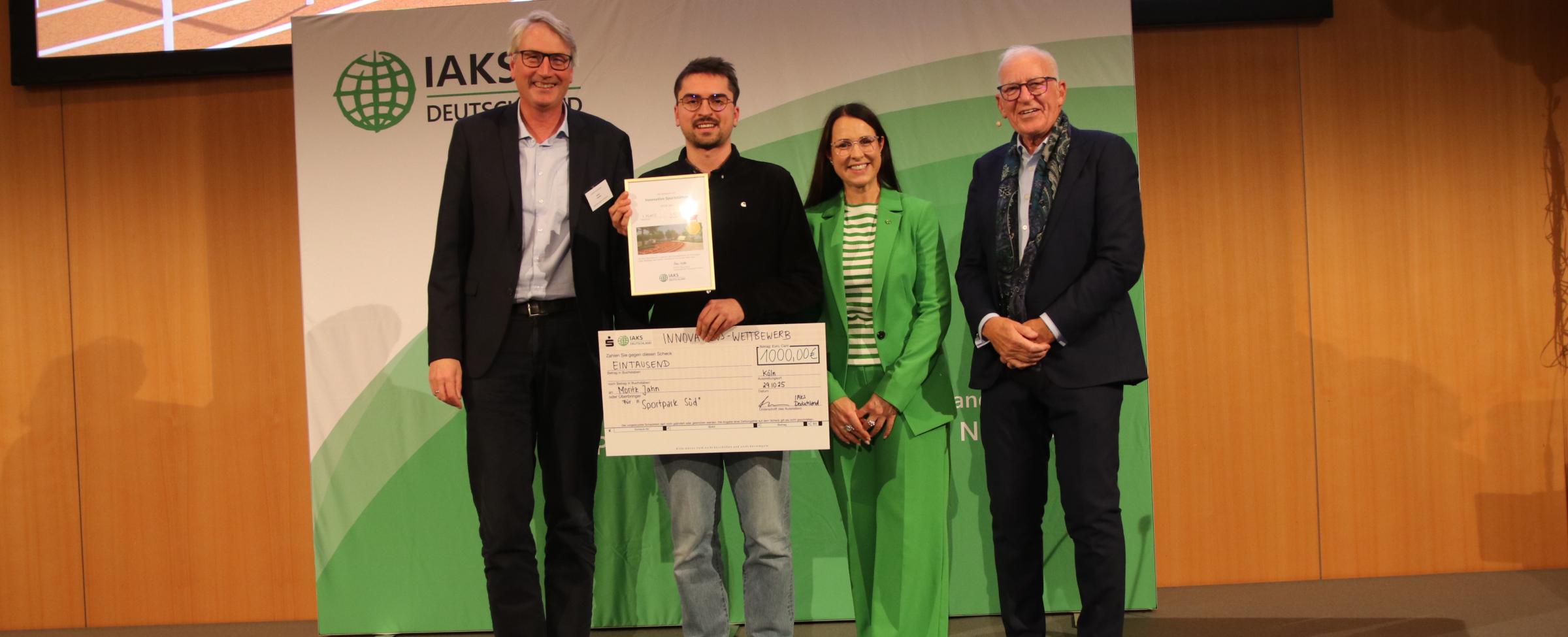 4 Menschen auf der Bühne, lächeln in die Kamer