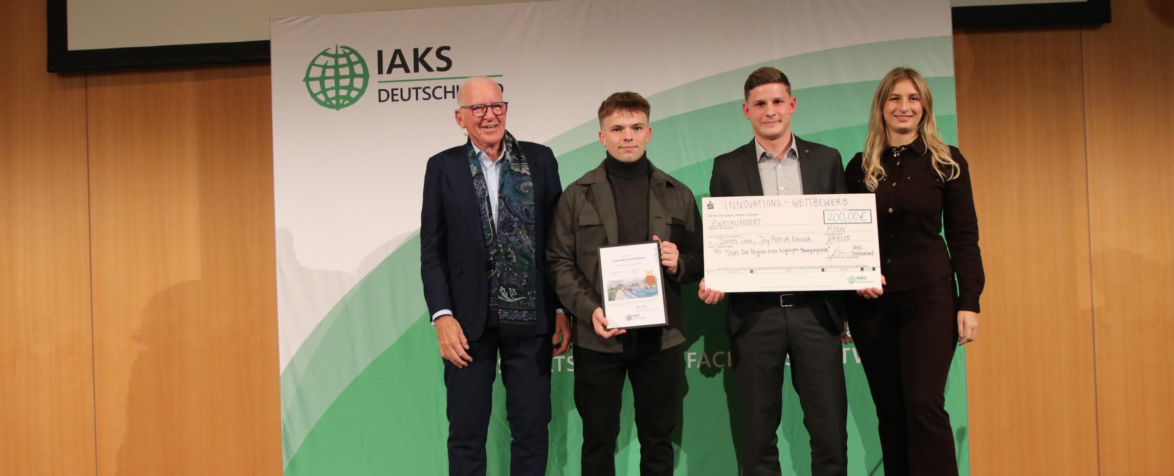 3 Menschen auf Bühne mit Urkunde und Scheck