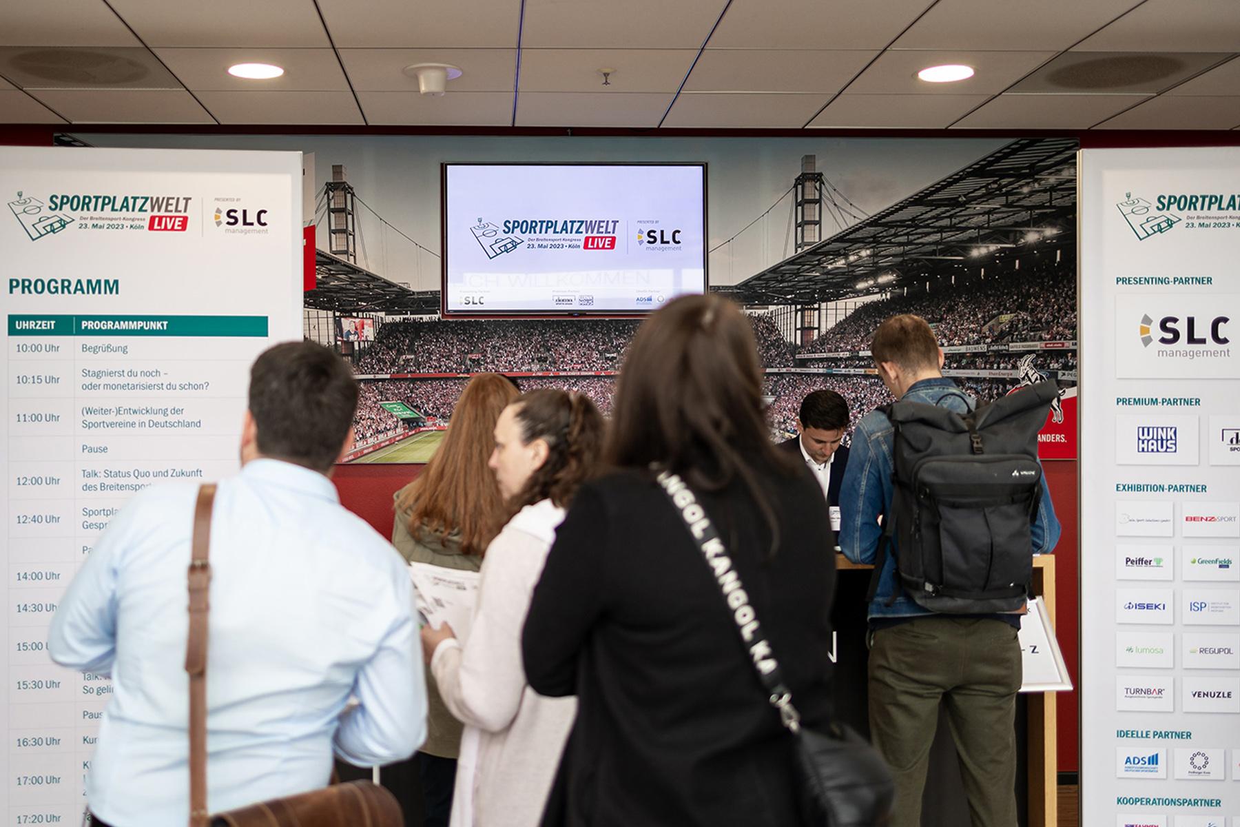 menschen vor sportplatzwelt live schild