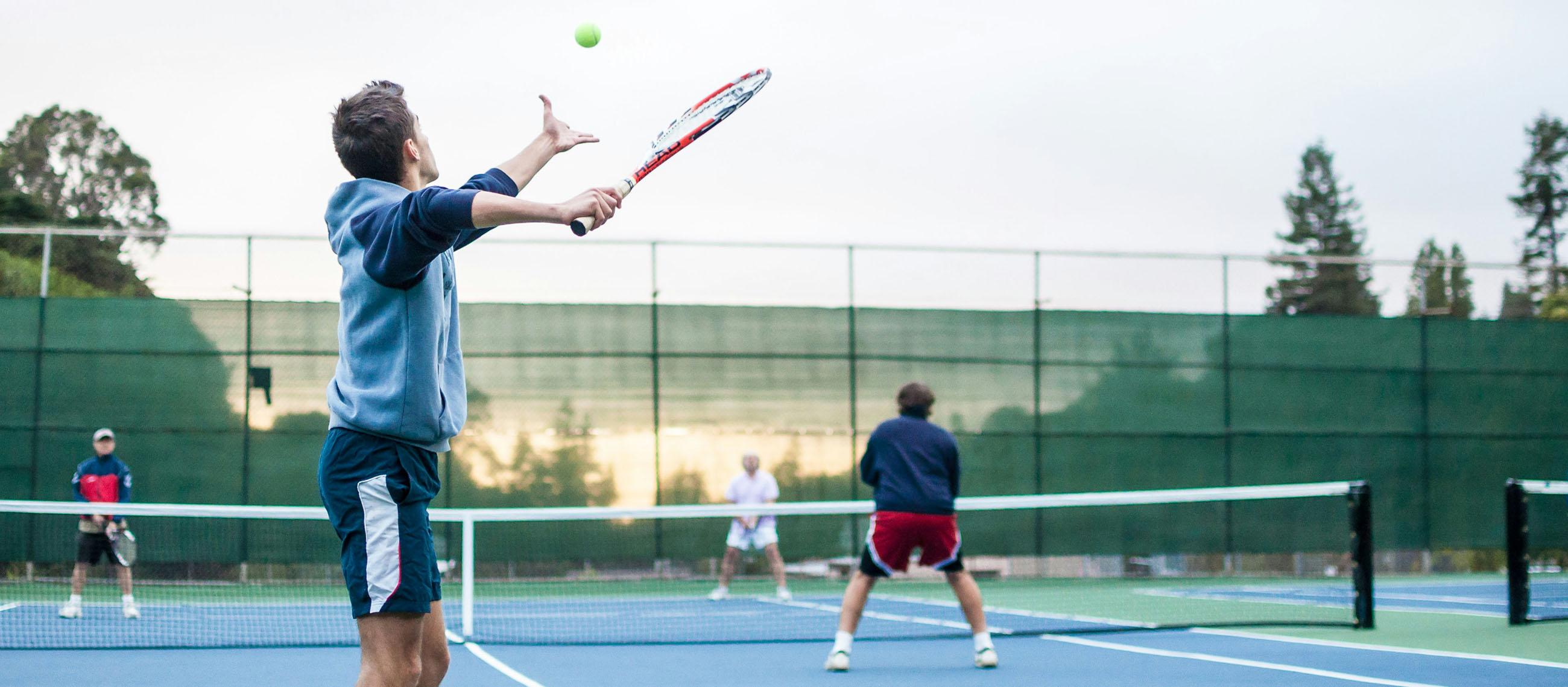 Mann steht auf Tennisplatz und schlägt auf