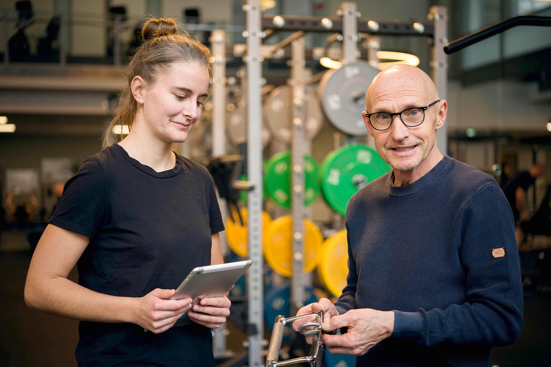 zwei Menschen prüfen ein Sportgerät, lächeln dabei in die Kamera
