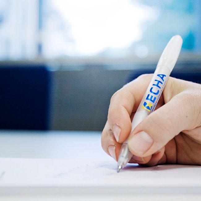Person writing with a pencil with the ECHA logo on it